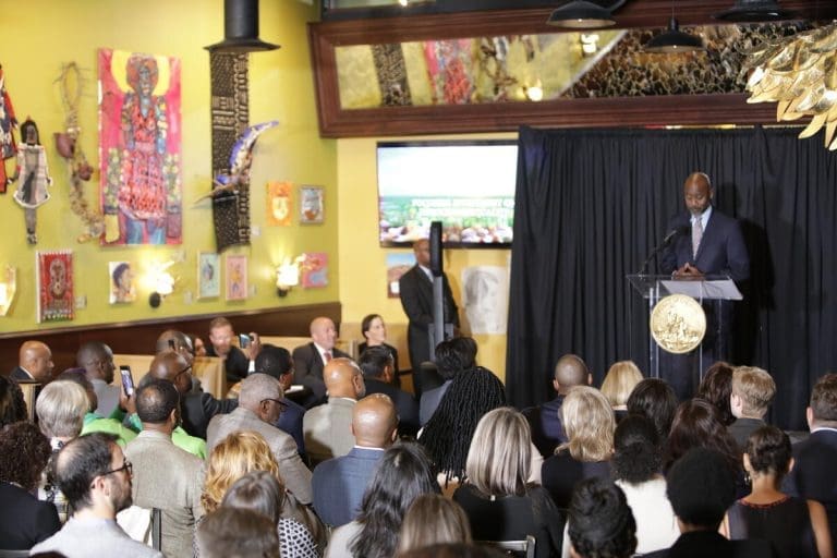 a man standing at a podium talking to men and women sitting in a crowd.