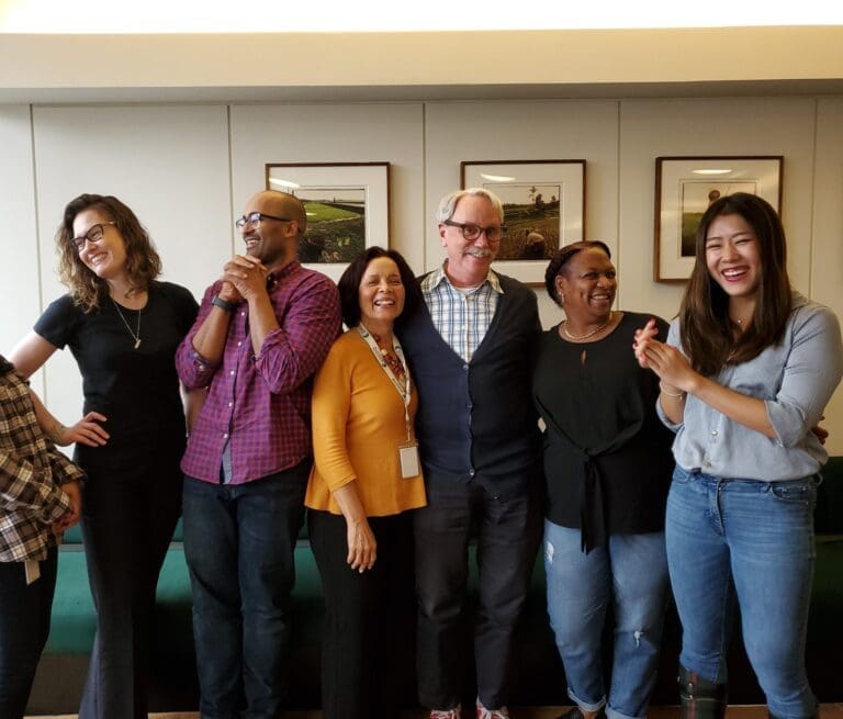 A group of men and women with their arms around each other laughing together.