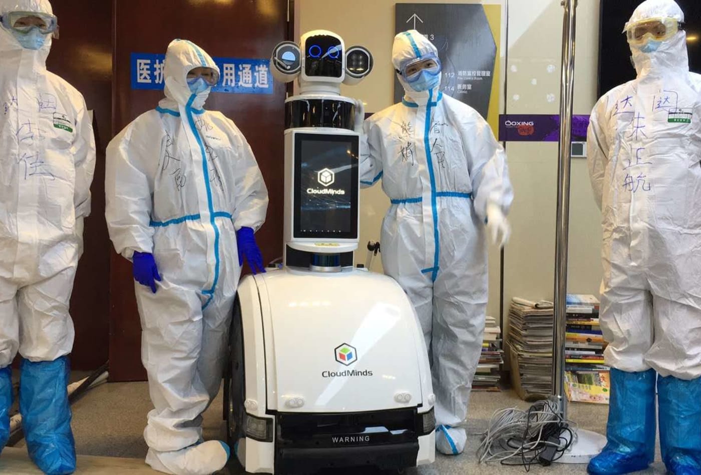 Healthcare workers in hazmat suits standing beside a robot designed to help them monitor Covid-19 patients.
