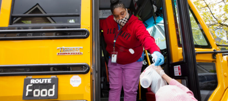 Female volunteer handing out meals from a school bus.