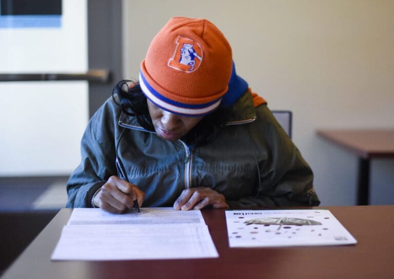 a woman sitting at a table looking down and writing on a piece of paper.