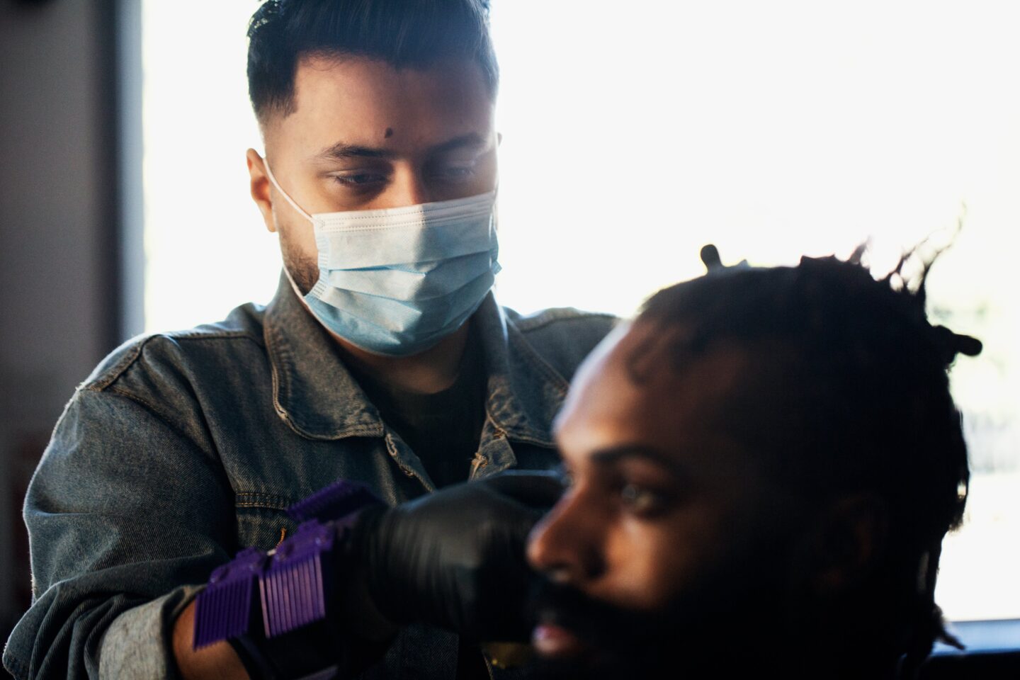 man wearing a facemask giving a man sitting a haircut