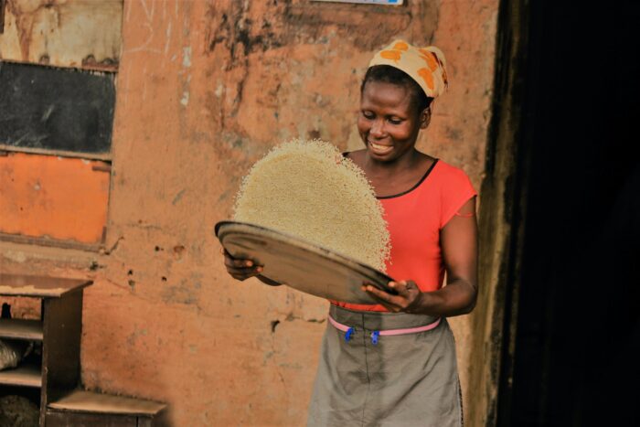woman standing and holding a tray mixing grains of rice.