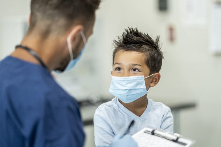 health worker looking at a young boy wearing a facemask.