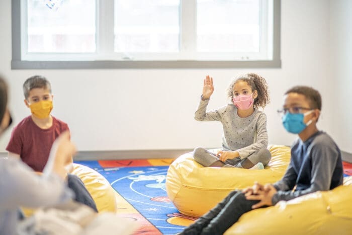 two young boys and a girl sitting in bean bags wearing facemasks.