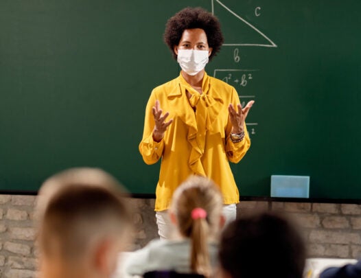 woman standing and teaching a class wearing a facemask.