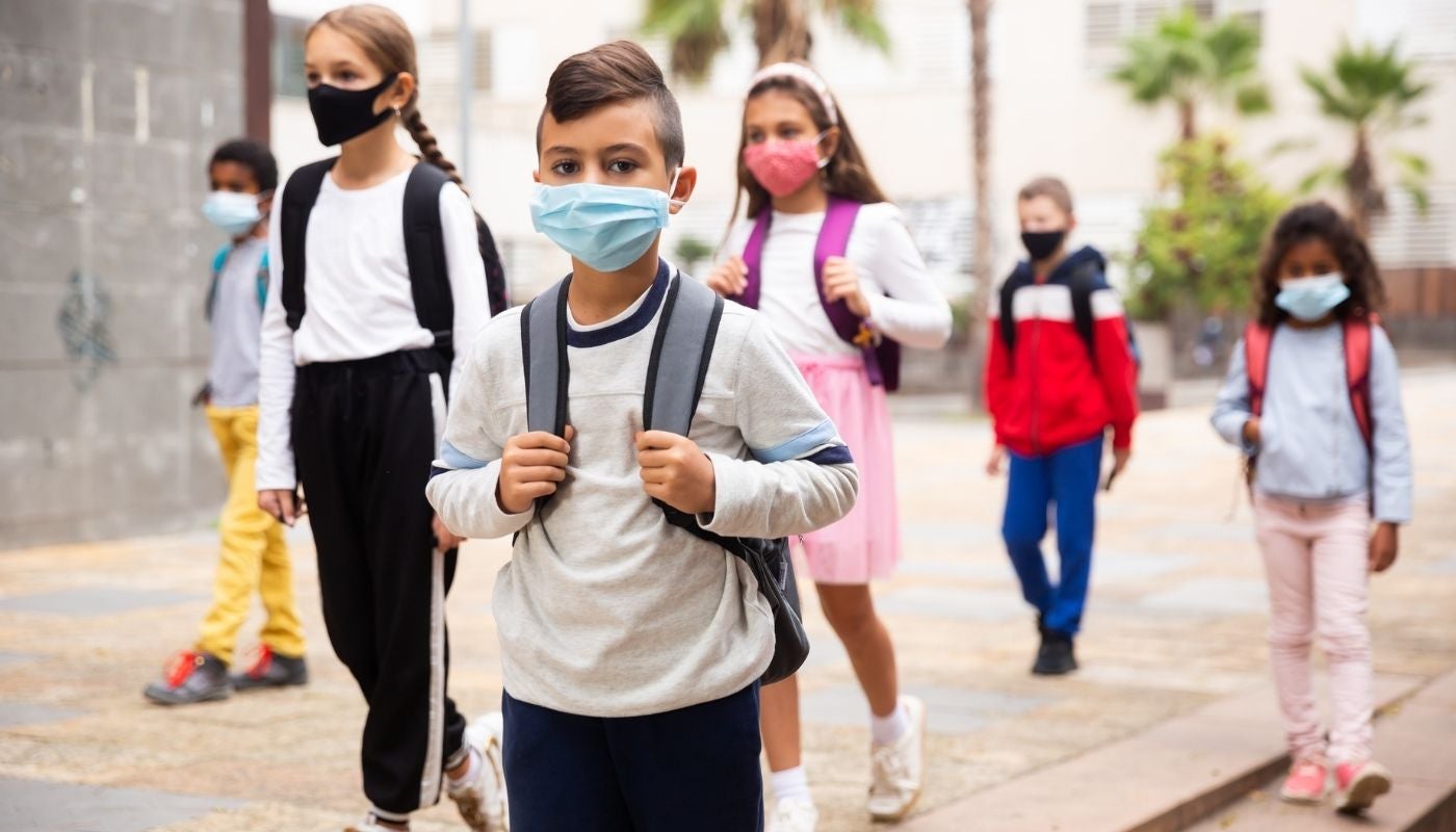 young boys and girls walking together wearing backpacks and facemasks.