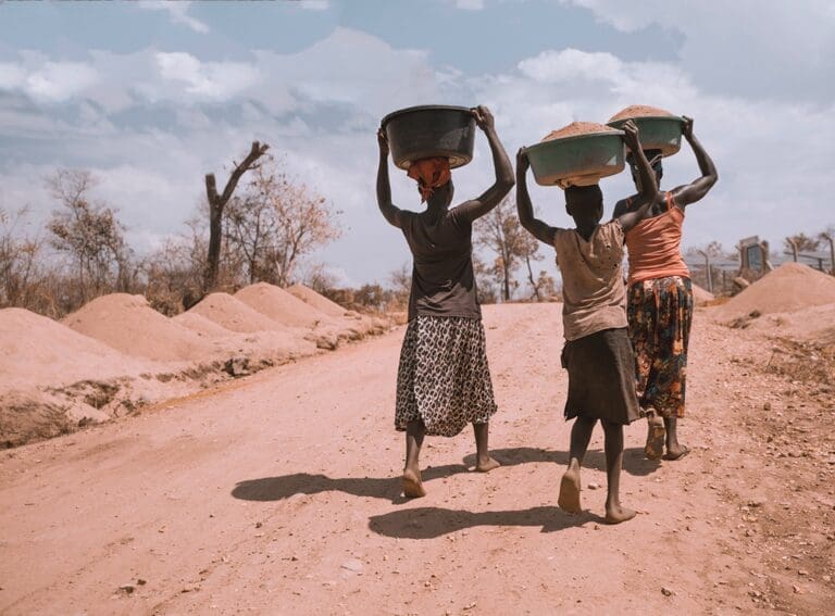 two women and a young boy carrying soil on top of their heads.