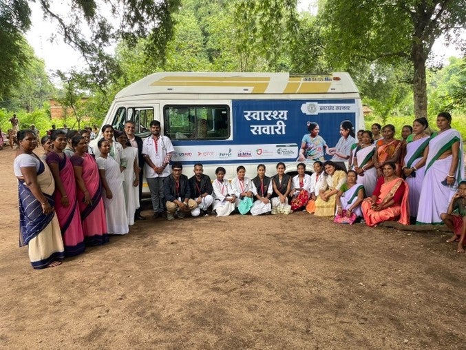 health workers pictured with men and women in a community in front of a medical van.