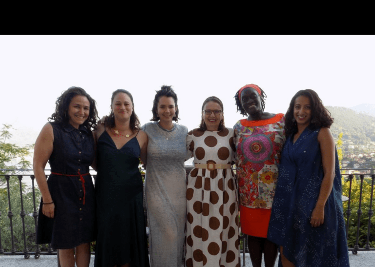 group of women standing outside on a balcony with their arms around one another smiling.