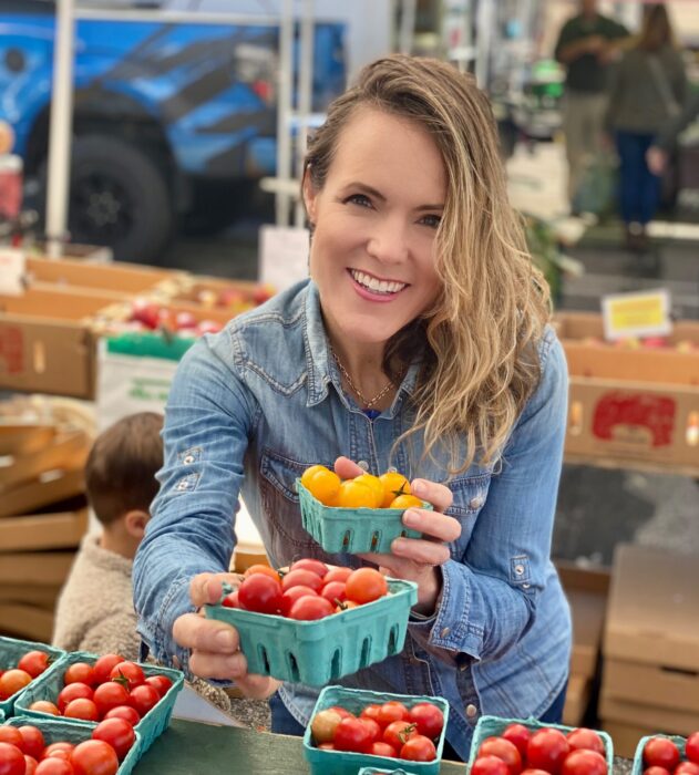 woman smiling at farmers market holding vegetables