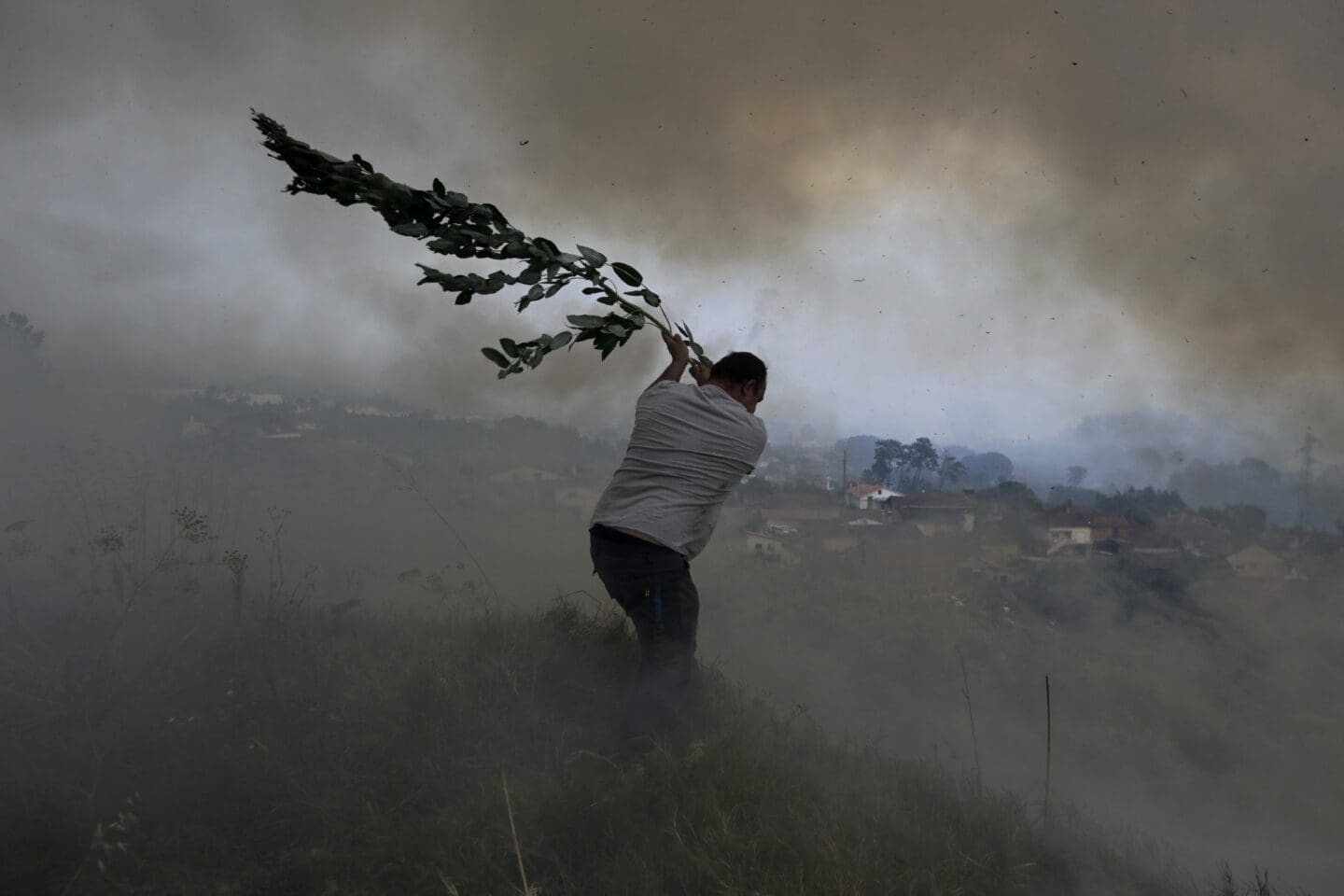 a man swinging a tree branch looking to stop or prevent a fire