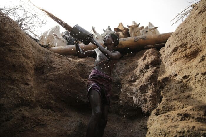 woman scooping water from a ground water well