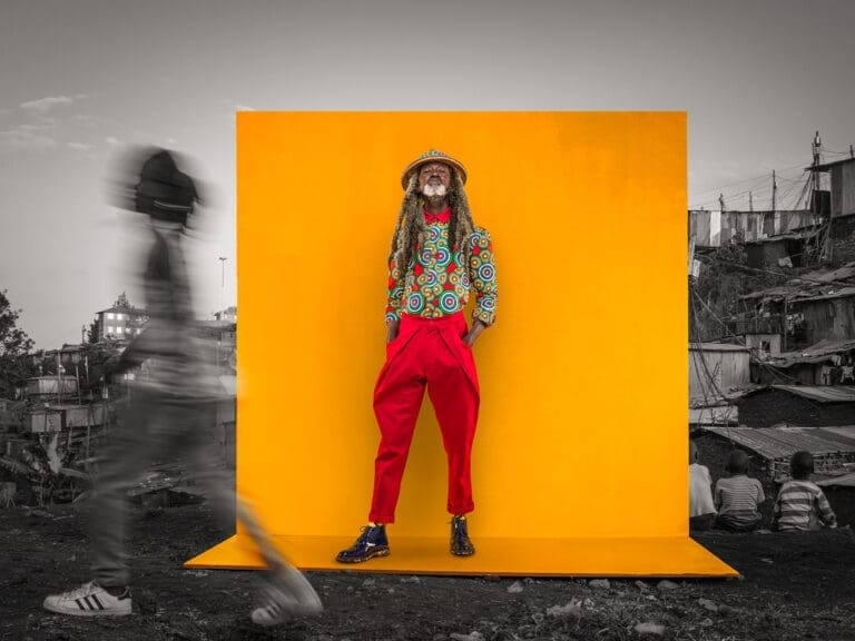 man standing with hands in his pockets in front of an orange back drop