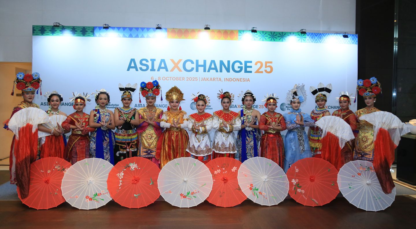 performers in traditional Indonesian costumes and ornate headdresses pose with decorative painted umbrellas in front of the AsiaXchange25 backdrop in Jakarta, Indonesia