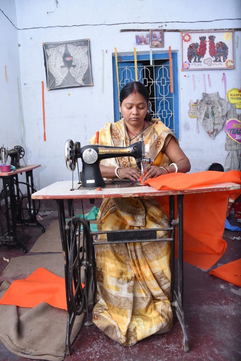 woman sitting in a chair using a manual sewing machine.