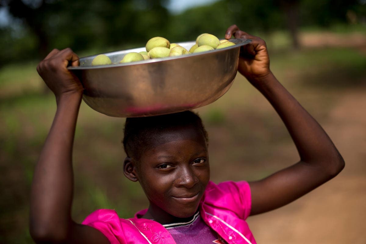 woman holding a basket of figs on top of her head.