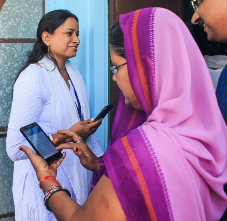 woman wearing a scarf scrolling through her phone with another woman across from her holding her phone and smiling