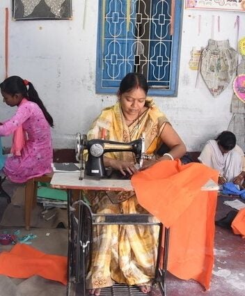 Three women using sewing machines to create dresses from colorful Indian fabric