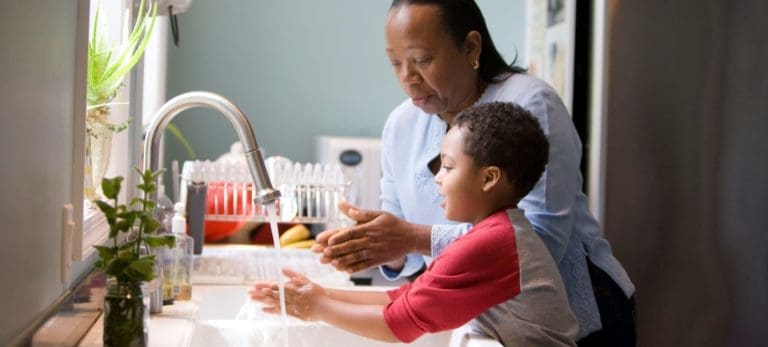 Woman showing a child how to wash his hands.