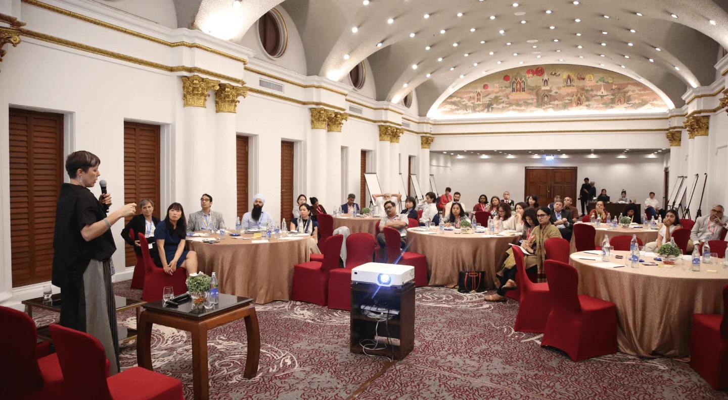 a spacious room filled with numerous people seated around various tables engaged in conversation.